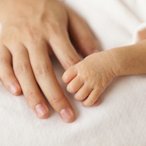 A preterm baby holds a parent's hand.
