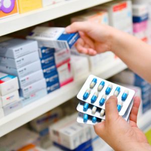 Person taking antibiotic pills off the shelf of a pharmacy.