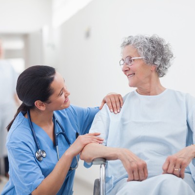 Female caregiver smiling at older, smiling female patient in wheelchair