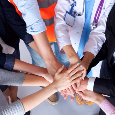 Several people, including a doctor, have their hands in a pile as if a team
