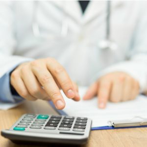 A doctor using a calculator to add up costs.