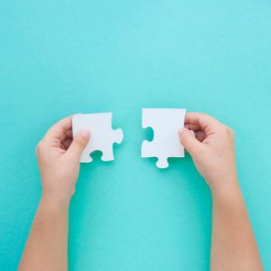 Child's hands hold two white puzzle pieces, a symbol of ASD.