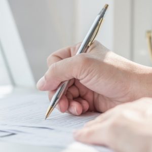 A person writing on paper with a silver pen.