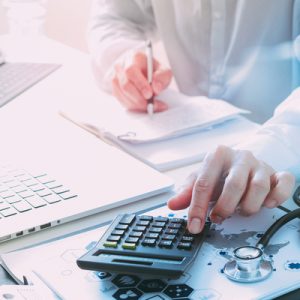 A person using a calculator with a stethoscope on the desk beside it.