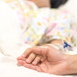 A person receiving acute care in a hospital holds the hand of another person.