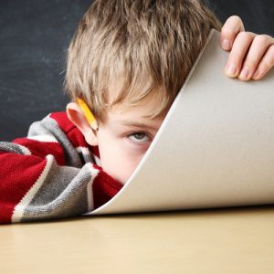 A white child with ADHD looks bored at a school desk.