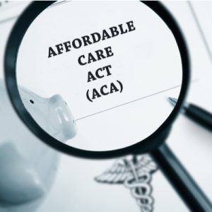 The words "Affordable Care Act (ACA)" in black on white paper under a magnifying glass.