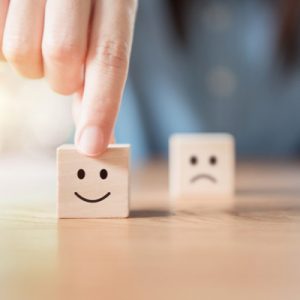 Two small blocks, one with a smiley face drawn in black and one with a frown face. A hand is moving the smiling block forward to show how health care satisfaction has increased since the implementation of the ACA.