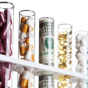 Test tubes, most filled with pills and one filled with money, indicating the rising cost of specialty drugs.