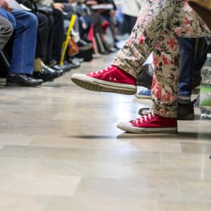 The feet and legs of many people sitting in chair in the waiting room of a primary care physician.