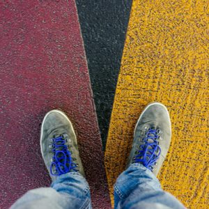 Two feet standing on a road, with a red stripe going one direction and a yellow stripe going the other direction, showing how Michigan health policy issues are at a crossroads.