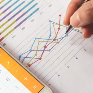 A hand holds a pen over a colorful chart with a calculator nearby, indicating the rate analysis of the health insurance marketplace.