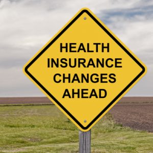 A yellow road sign reading, "Health insurance changes ahead," indicating changes due to the health care proposals the author is comparing.