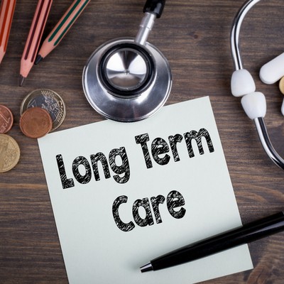 Paper that reads Long Term Care is on table with stethoscope, coins and pencils
