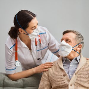 Nurse wearing a mask cares for an elderly man wearing a mask in a nursing home.