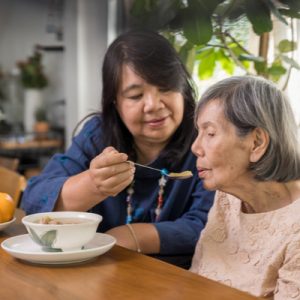 An unpaid caregiver feeds her mother soup.