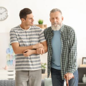 A caregiver supports the arm of an older man using a cane.