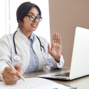 A physician waves at a laptop while providing telehealth services.