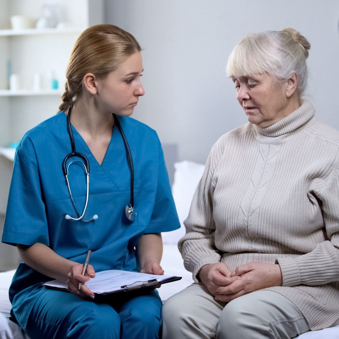 Female health care worker filling out chart of adjacent older female