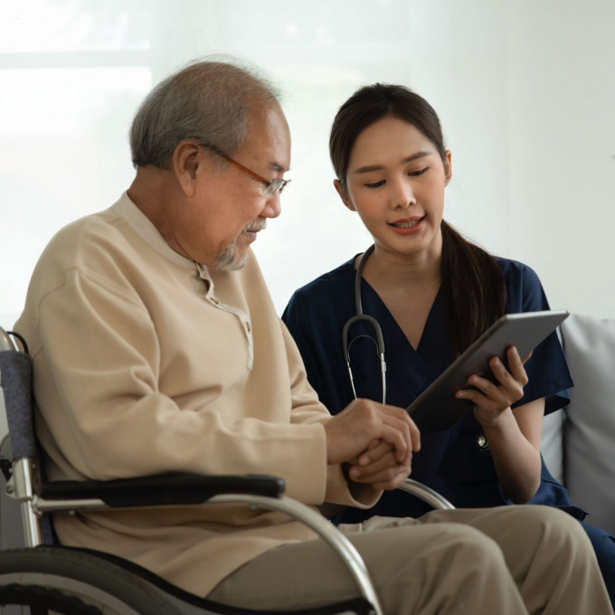 A doctor and a patient in a wheelchair look at a chart together.