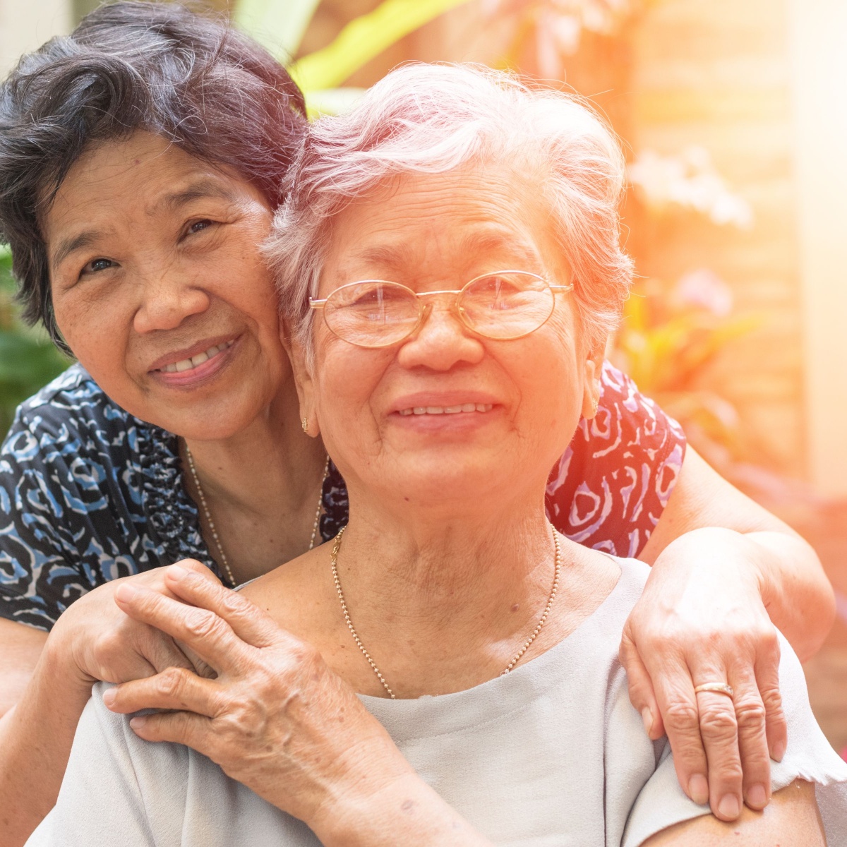 An older Asian woman in a wheelchair holds hands with her caregiver.