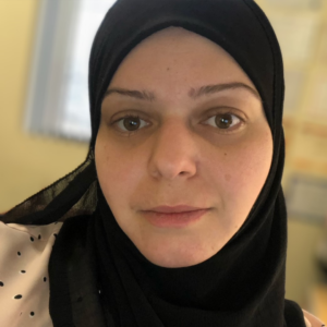 Houda wearing a black headscarf with a window in the background.