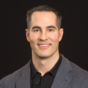 Sean in a gray blazer and black shirt against a black backdrop.