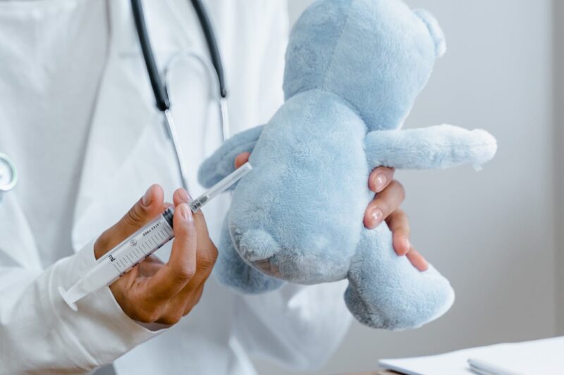 Doctor demonstrates a vaccine on a blue teddy bear